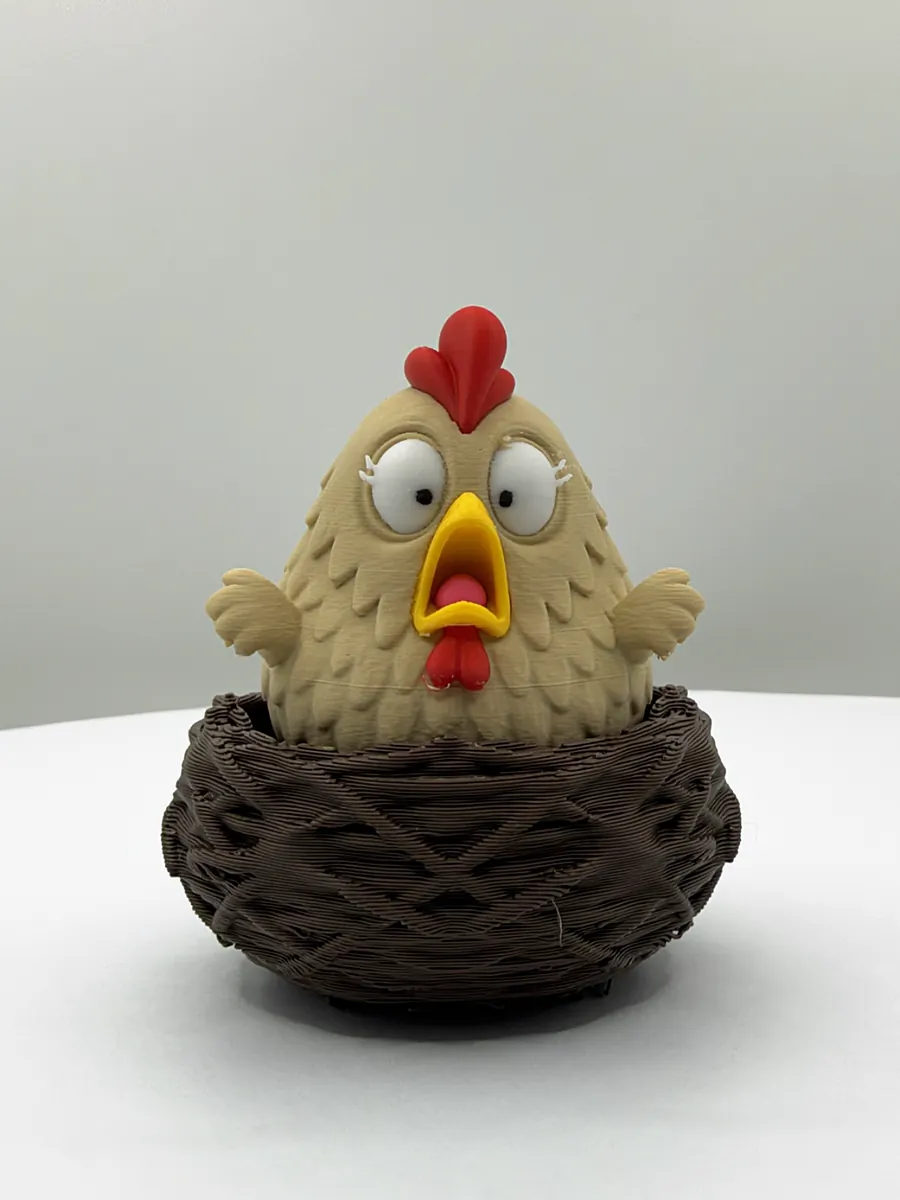 The Chicken Nest Clicker in a dark brown nest from the front: cream with a red comb and an open beak